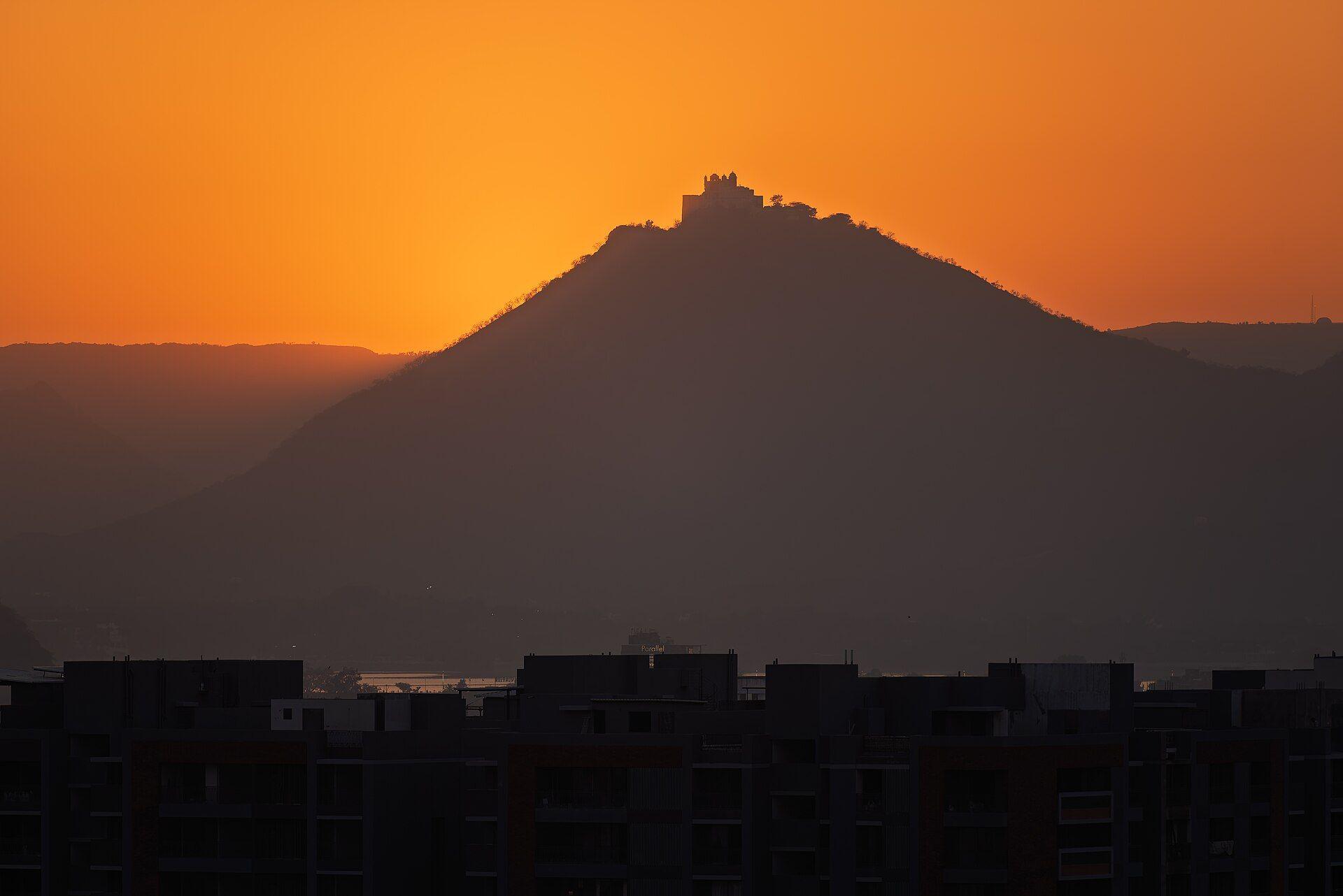Sajjangarh, the Monsoon Palace, silhouetted on its hilltop against an orange sunset sky.