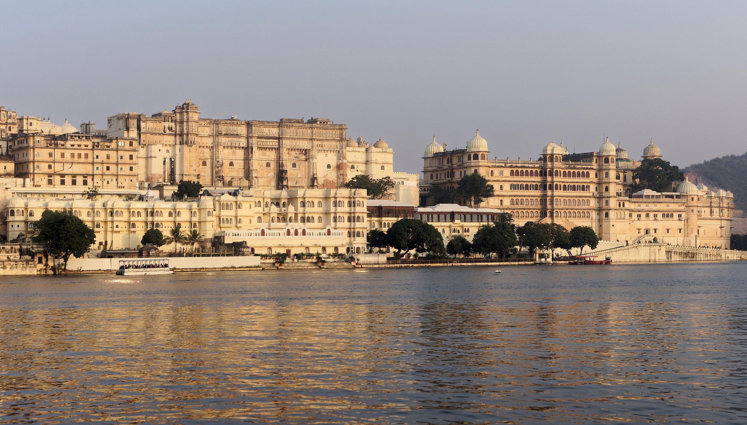 The City Palace of Udaipur glowing in low evening light above the still water of Lake Pichola.