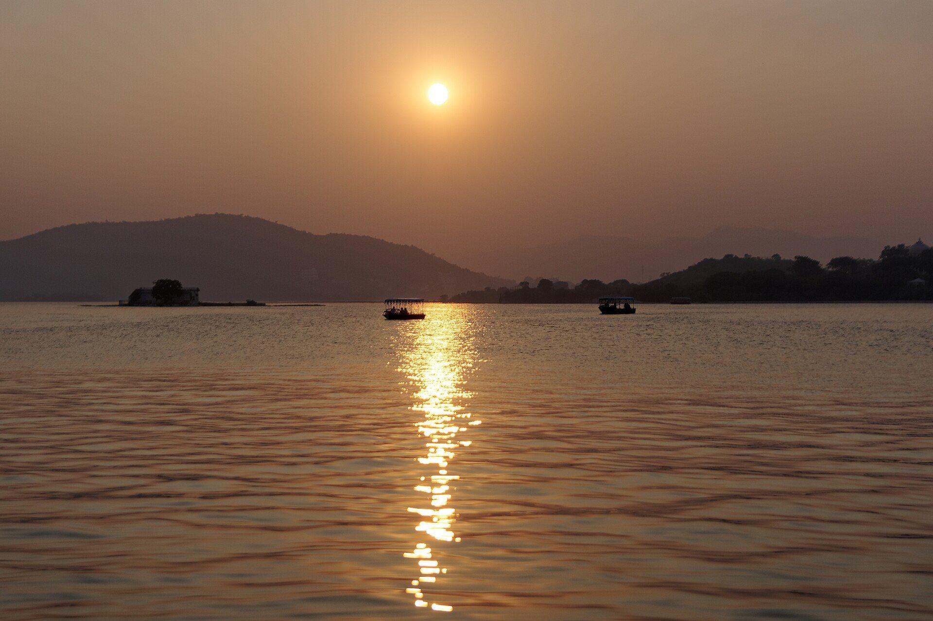 Sun glitter on the water of Lake Pichola at sunset, with hills on the far shore.