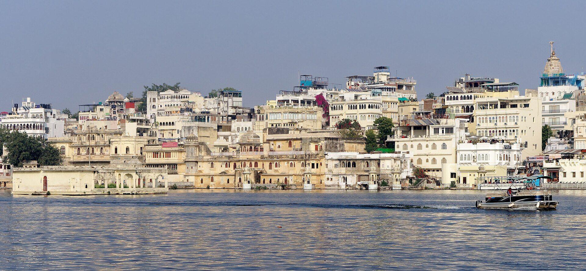Old houses rising from the shore of Lake Pichola in Udaipur, with the pavilion of Mohan Temple at the water's edge and a temple spire behind.