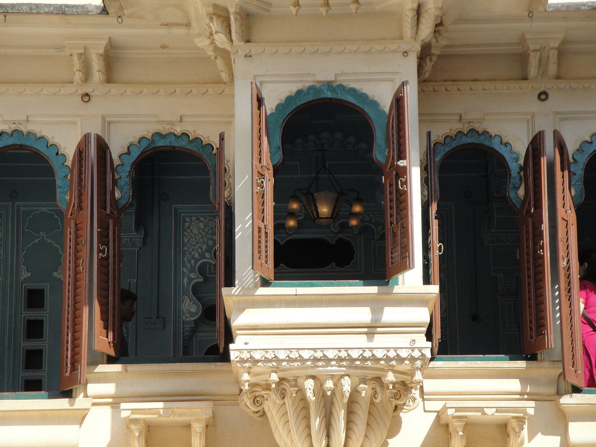 Arched windows with open wooden shutters on the cream stone facade of the City Palace in Udaipur.