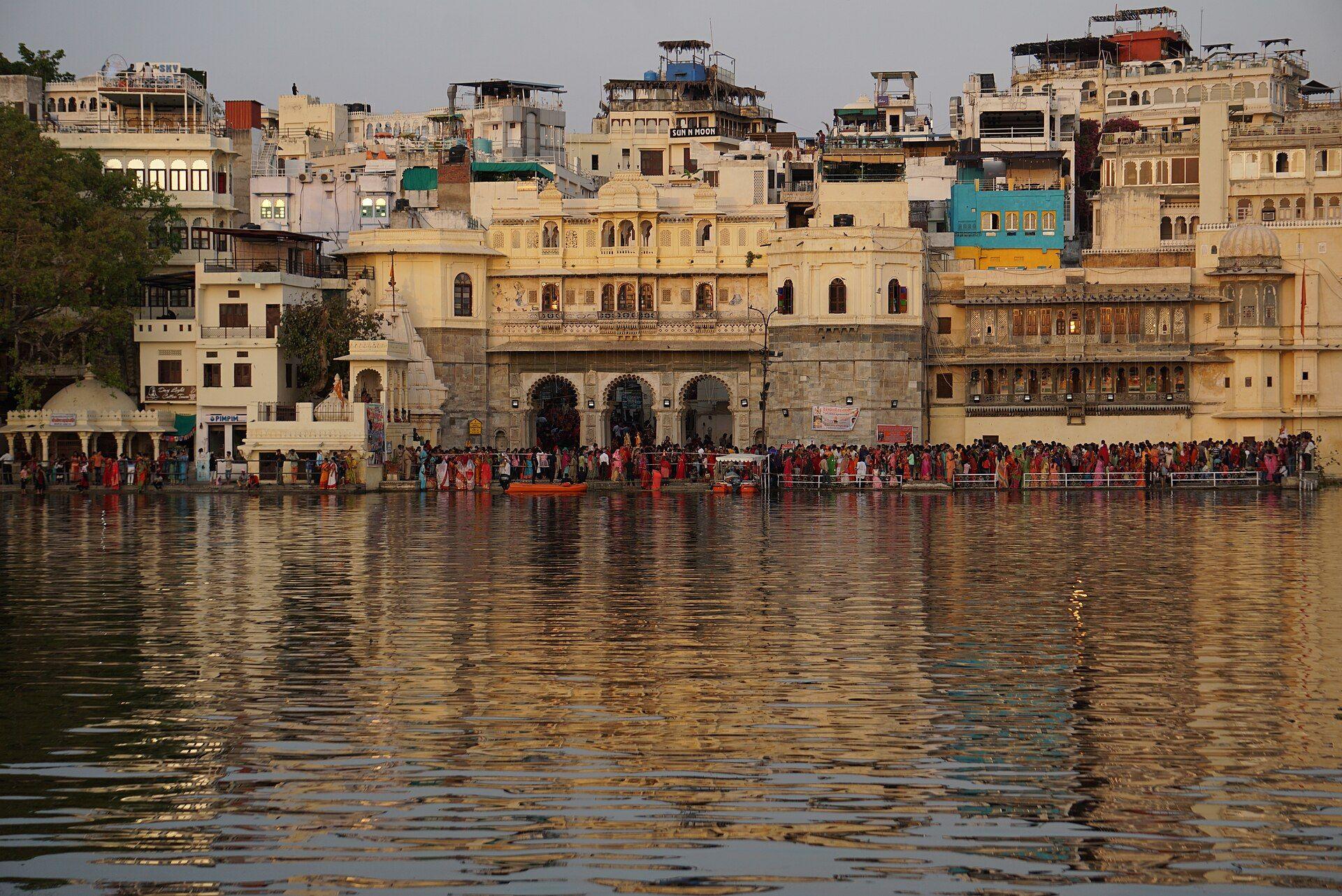 Gangaur Ghat on Lake Pichola at golden hour, the old city's arched frontage reflected in the water.